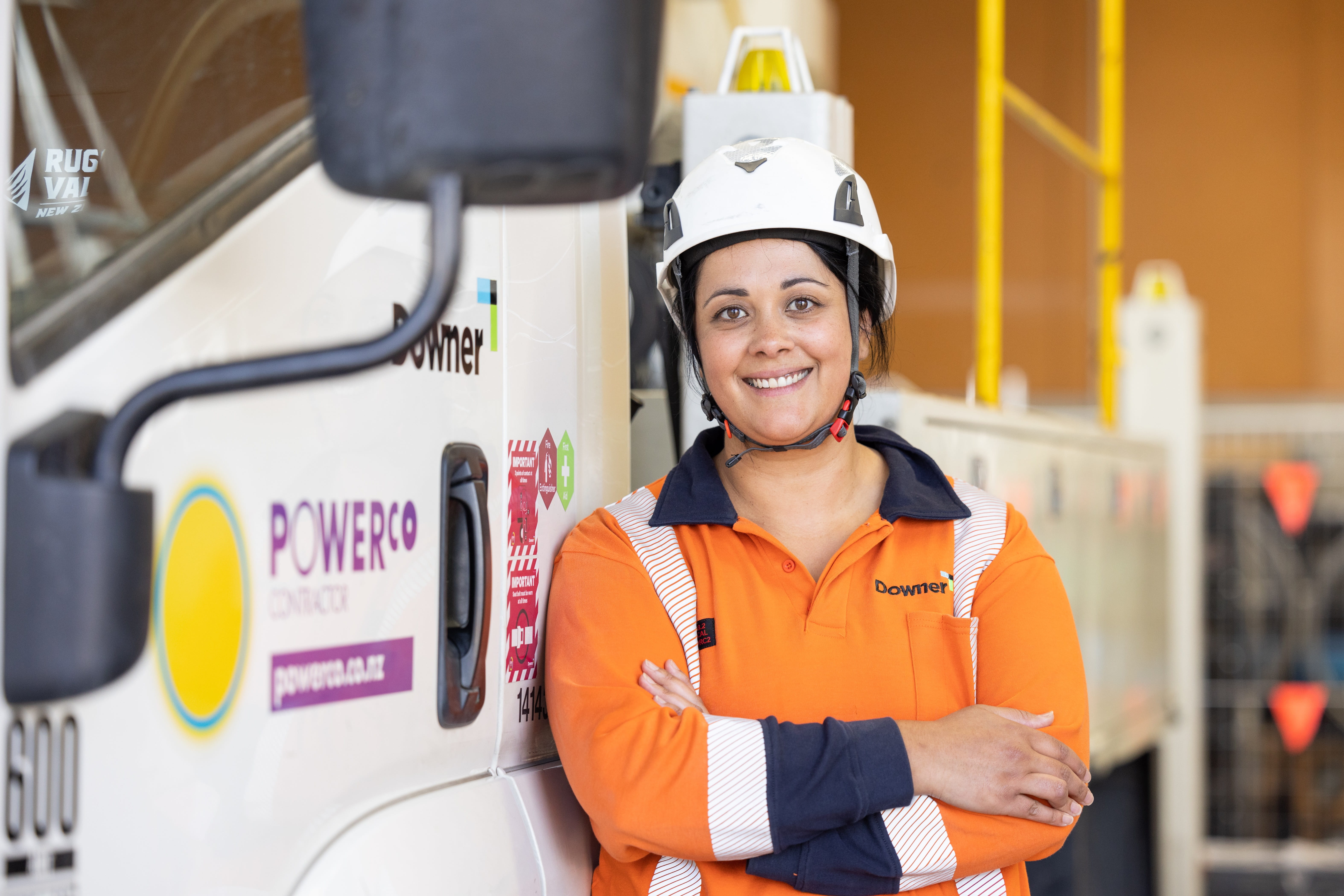 A female power line mechanic with helmet and PPE on, smiling and posing beside a work truck