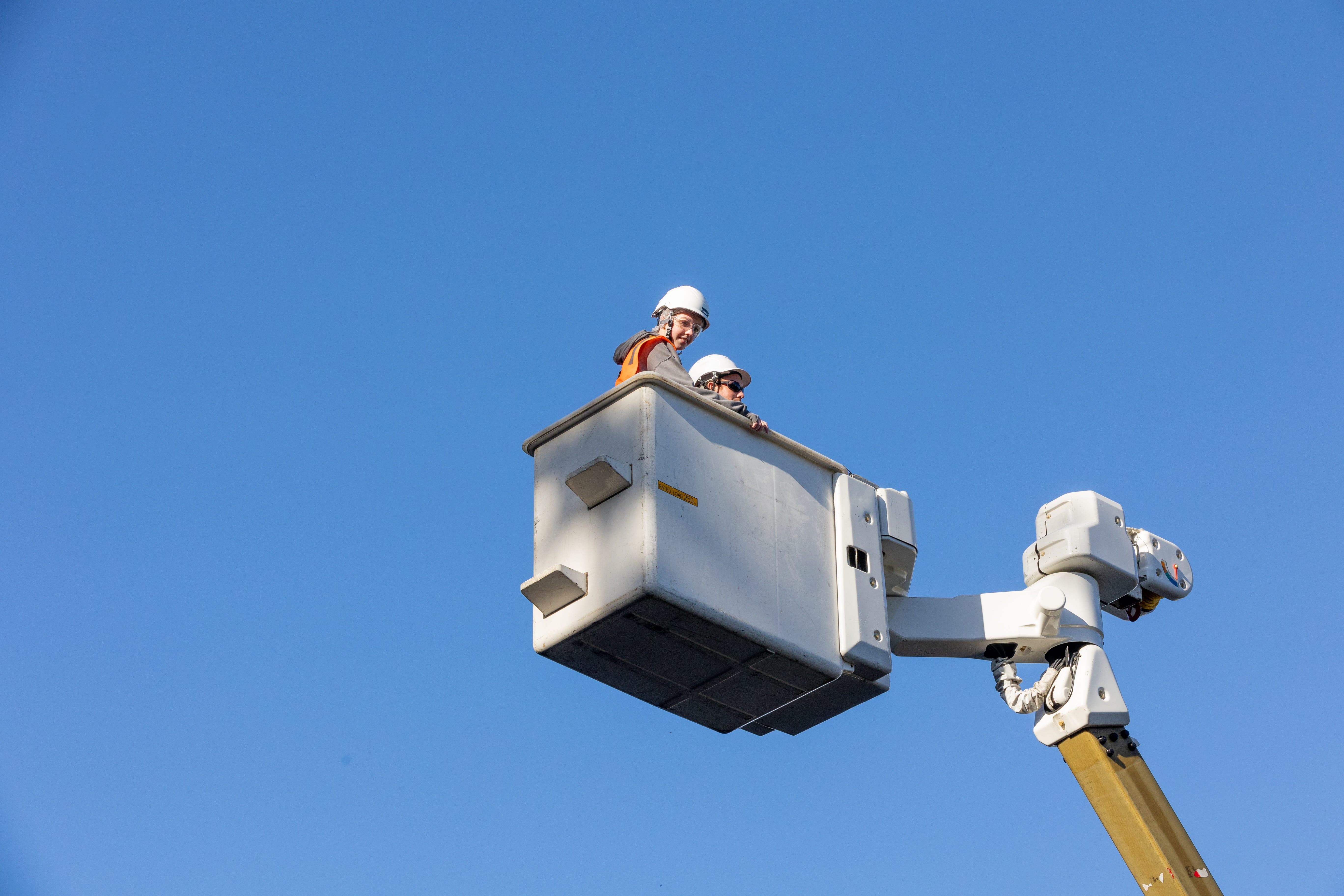 Electricity faultman and female student up high in the bucket of a truck with blue sky as the background