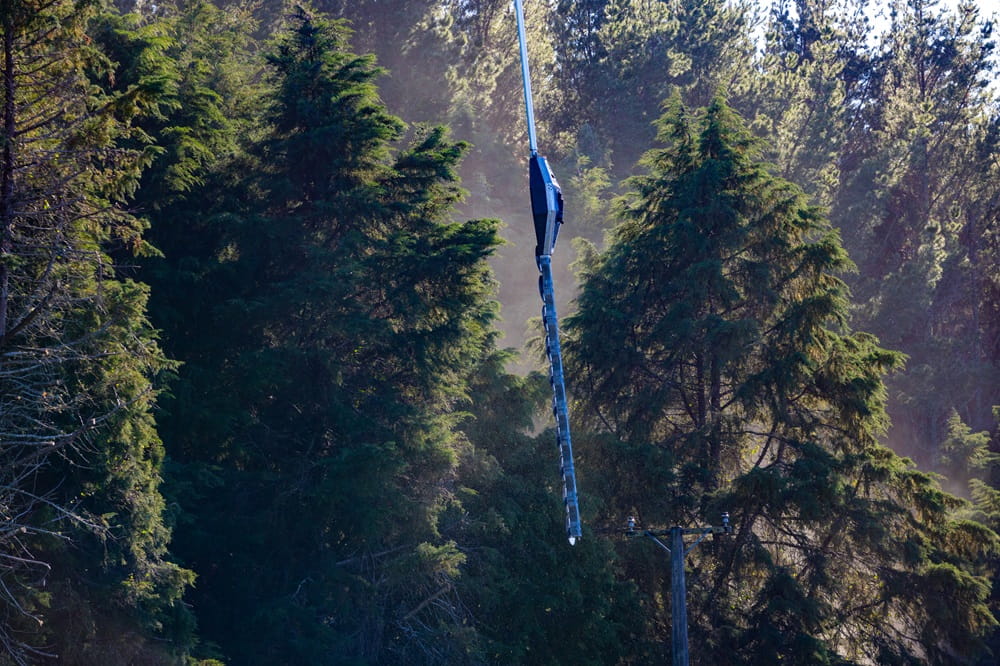 Close up of a saw being suspended from a helicopter in a pine forest