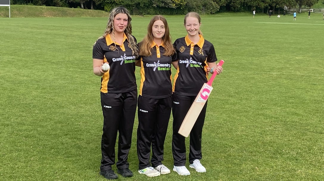 Three teenage women wearing black cricket uniforms